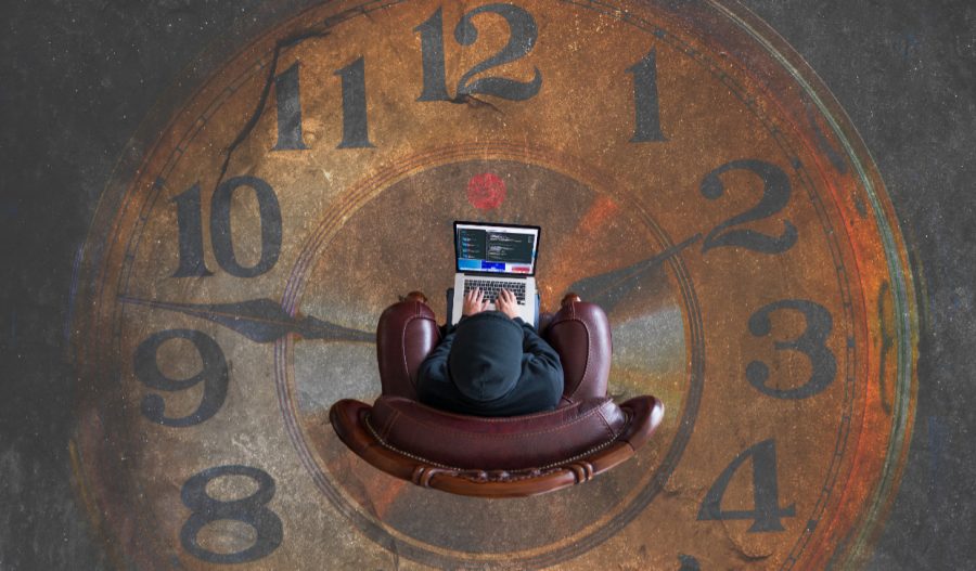 Image of a man sitting in an armchair with a laptop, in the middle of a clockface painted on the floor.